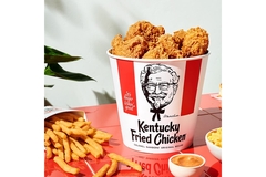 Image KFC fried chicken bucket with fries and sauces next to it.